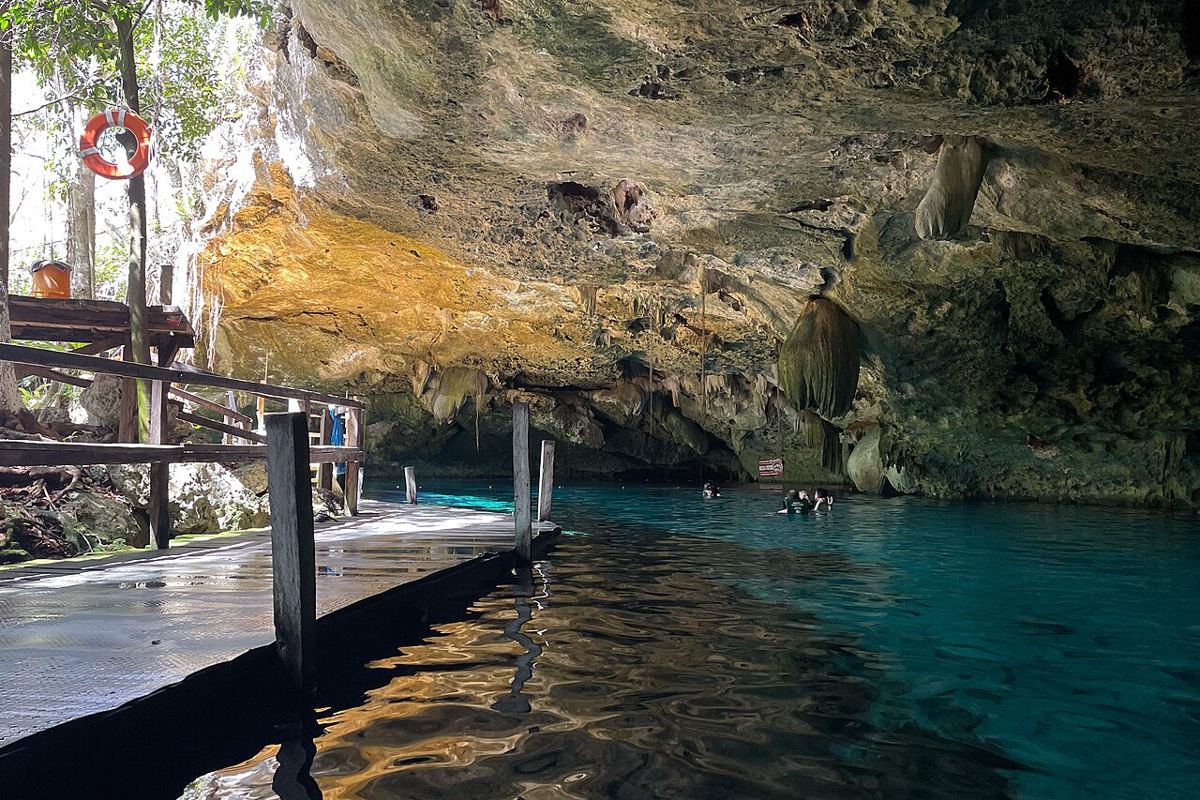 Agua turquesa y pasarela de madera bajo la bóveda de roca del cenote Dos Ojos